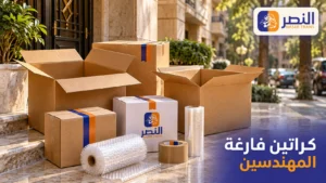 كراتين فارغة بأحجام مختلفة مع بابلز واسترتش وشريط تغليف أمام مدخل عمارة، بتصميم يحمل شعار النصر وعنوان كراتين فارغة المهندسين.